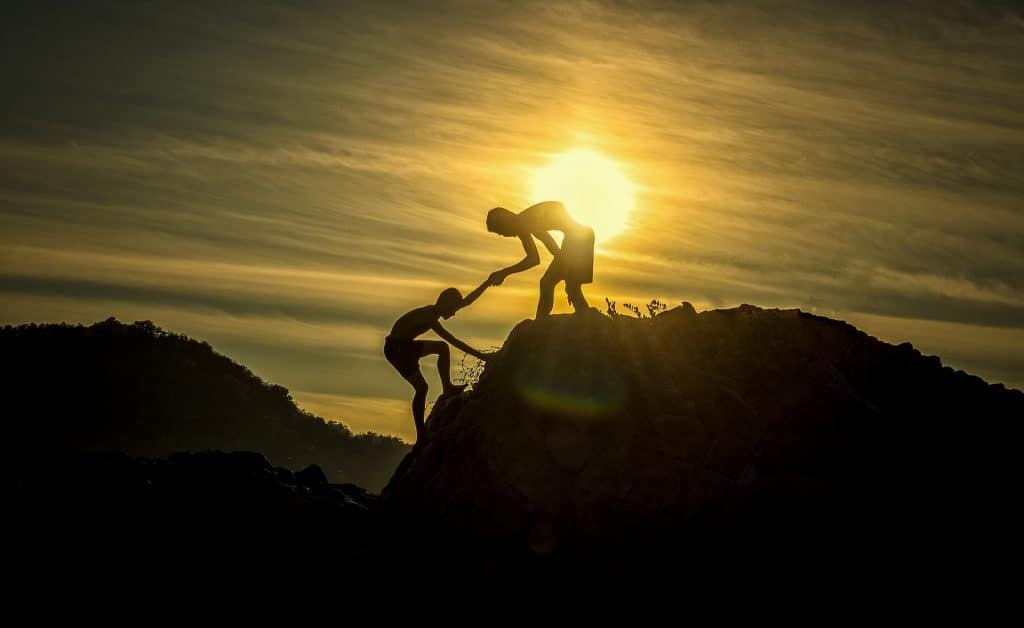 une personne au sommet d'une colline tend la main à une autre personne pour l'aider à grimper